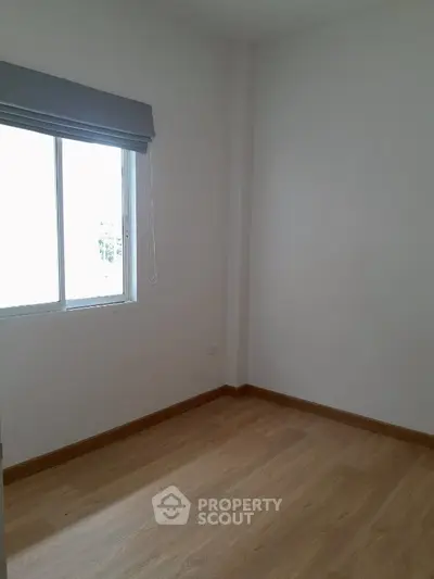 Bright empty room with wooden flooring and large window, perfect for customization.