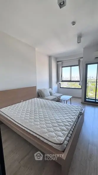 Modern bedroom with large window and city view, featuring a cozy seating area and minimalist design.