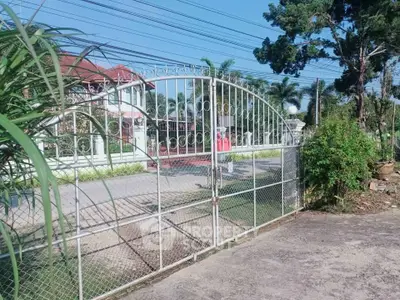 Charming gated entrance to a spacious property with lush greenery and a welcoming driveway.