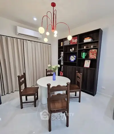 Charming dining area with modern chandelier and stylish bookshelf, perfect for cozy gatherings.