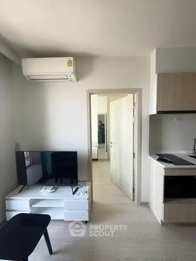 Modern living room with air conditioning and sleek kitchen area in a compact apartment.