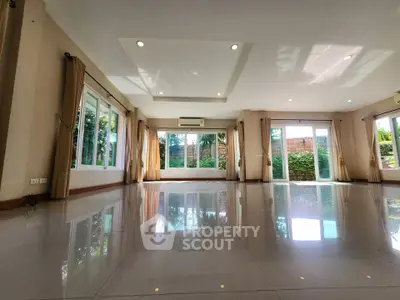 Spacious living room with large windows and polished tile flooring, offering abundant natural light and garden views.