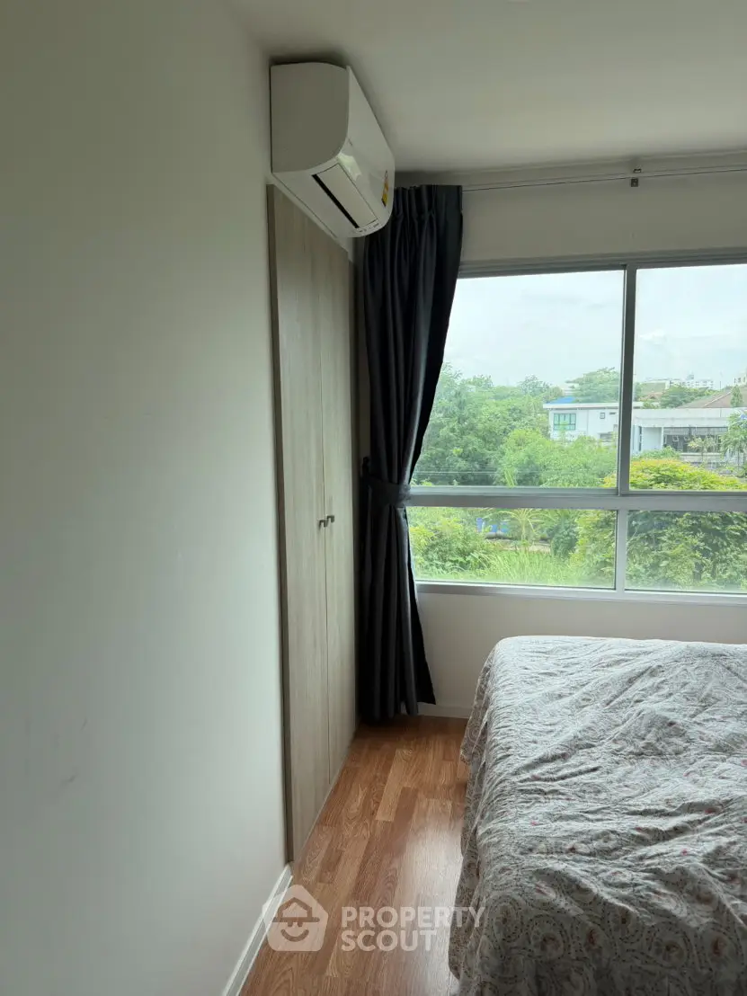 Cozy bedroom with large window and air conditioning, offering a serene view of lush greenery.