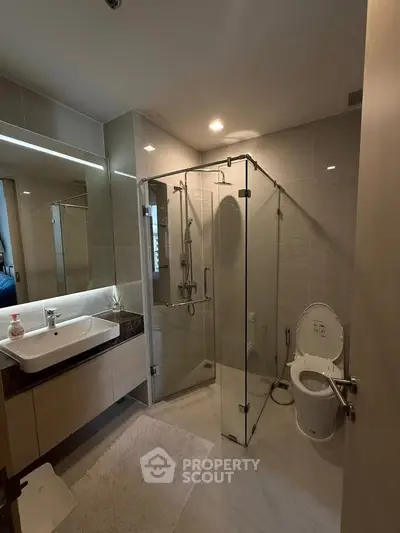 Modern bathroom with glass shower enclosure and sleek vanity in a contemporary apartment.