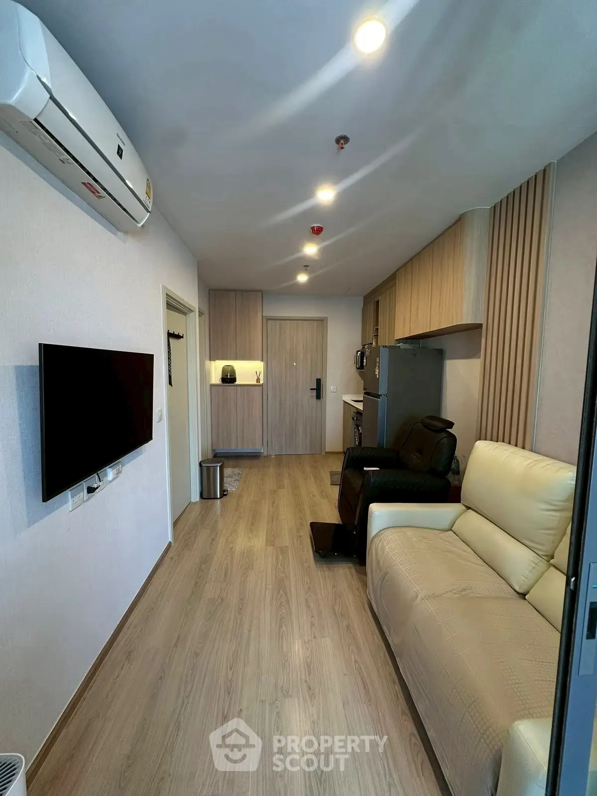 Modern living room with sleek design, featuring a comfortable sofa, wall-mounted TV, and stylish kitchen area.