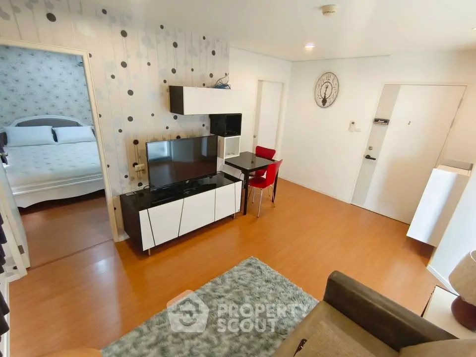 Modern living room with stylish decor and adjacent bedroom, featuring sleek furniture and wooden flooring.