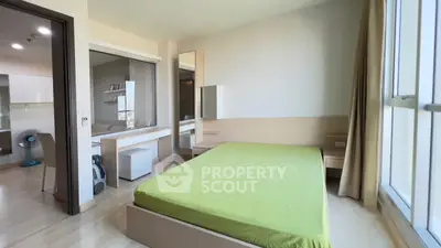 Modern bedroom with green bedding, large window, and sleek furniture in a bright apartment.