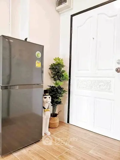 Modern kitchen corner with sleek fridge and decorative plant beside elegant white door.