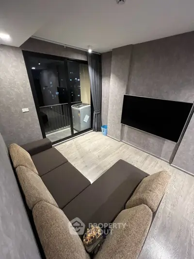 Modern living room with large sofa and wall-mounted TV, featuring a balcony view.