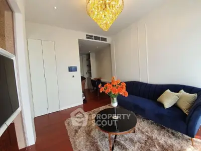 Elegant living room with plush blue sofa, chandelier, and cozy rug in modern apartment.