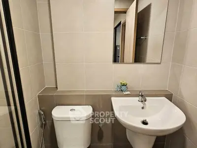 Modern bathroom with sleek fixtures and neutral tiles, featuring a compact sink and toilet.