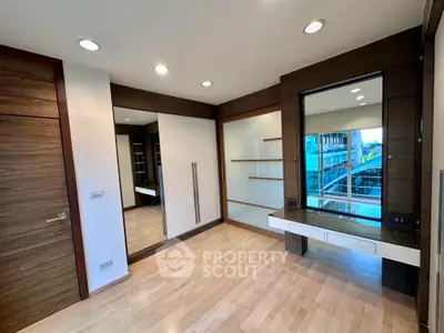 Modern bedroom with wooden flooring and built-in wardrobe, featuring large mirror and ample natural light.