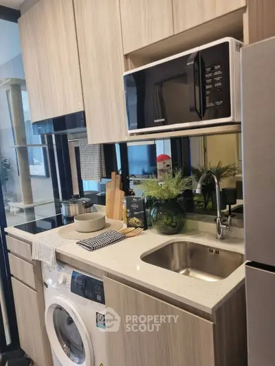 Compact modern kitchen with washing machine and microwave in stylish apartment.