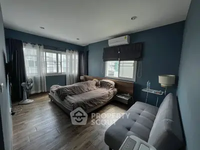 Spacious bedroom with modern decor, featuring a cozy bed, stylish sofa, and large windows for natural light.