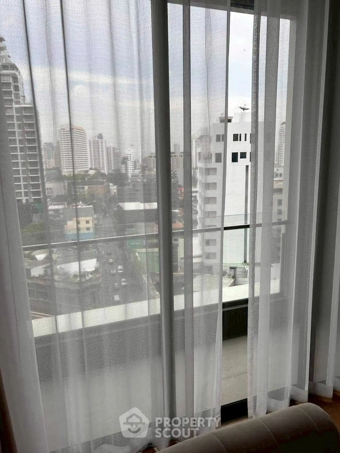 Stunning cityscape view from a high-rise apartment window with sheer curtains and balcony.