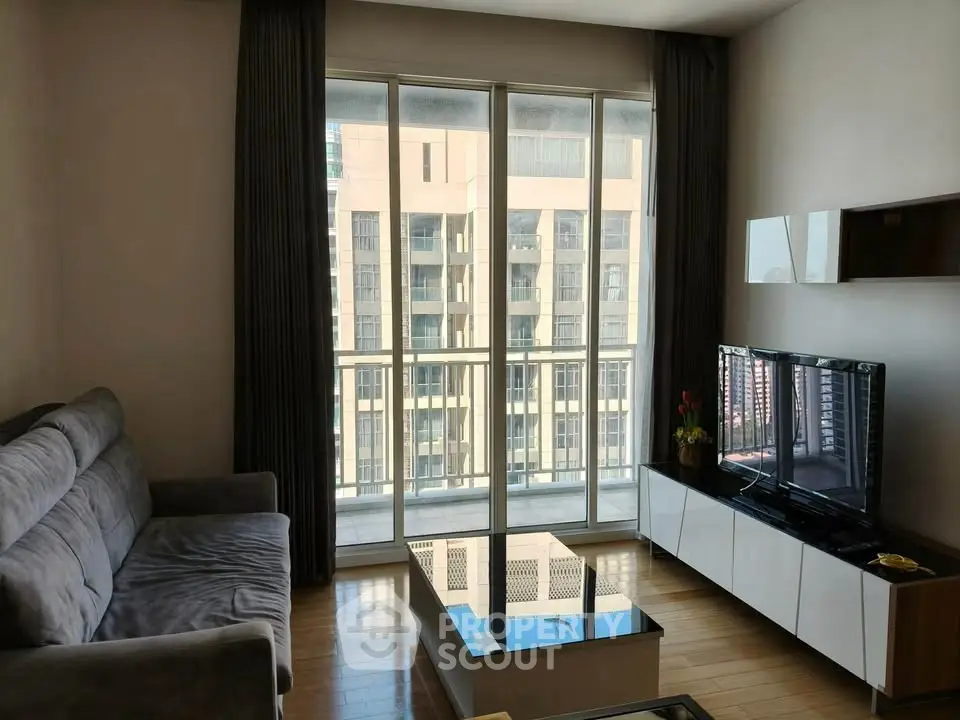 Modern living room with large windows and city view, featuring a cozy sofa and sleek TV setup.