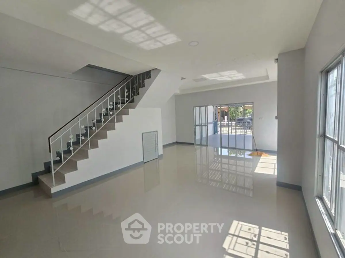 Spacious modern living room with sleek staircase and large windows for natural light.