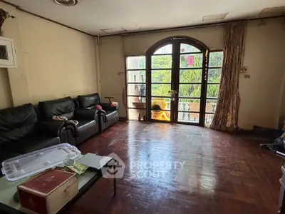 Spacious living room with wooden flooring and large arched window overlooking greenery.