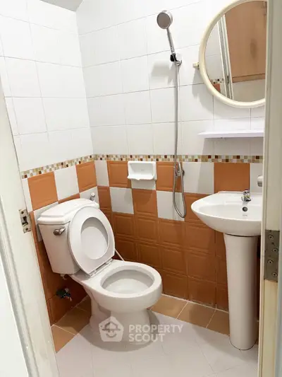 Compact bathroom with orange and white tiles, featuring a toilet, pedestal sink, and showerhead.