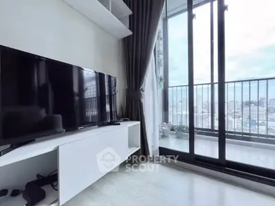 Modern living room with balcony and city view, featuring sleek TV setup and floor-to-ceiling windows.