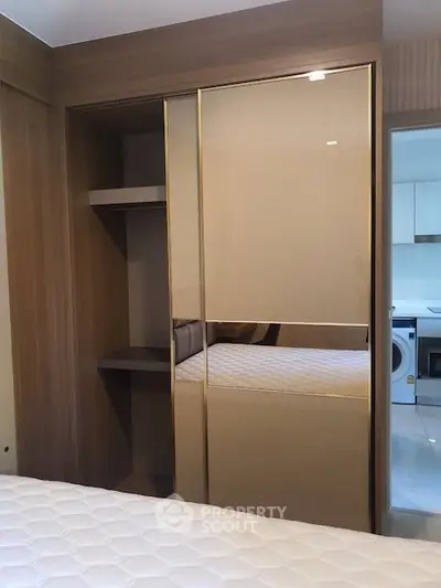 Modern bedroom with built-in wardrobe and partial view of kitchen appliances.