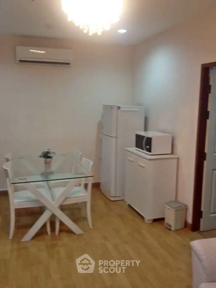 Cozy dining area with modern glass table, air conditioning, and kitchen appliances in a stylish apartment.