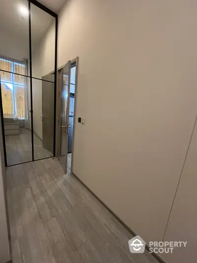 Spacious and modern hallway with elegant wood flooring and large mirrored closet doors reflecting a well-lit room, perfect for contemporary living.