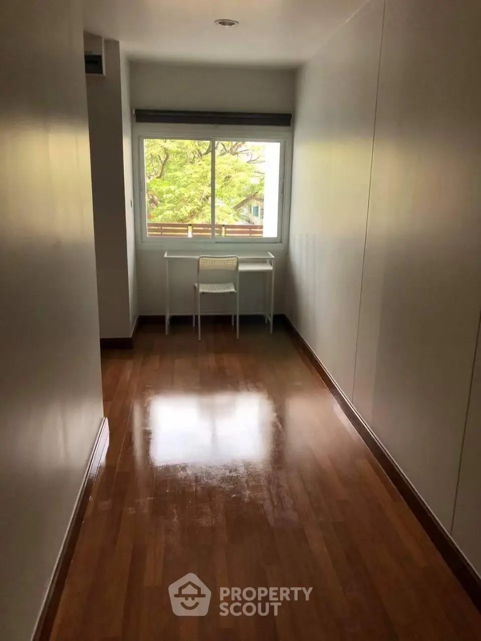 Bright study room with wooden flooring and large window offering lush green views.