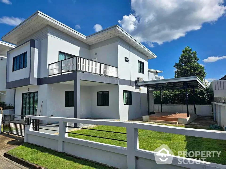 Modern two-story house with spacious backyard and covered parking area under clear blue sky.