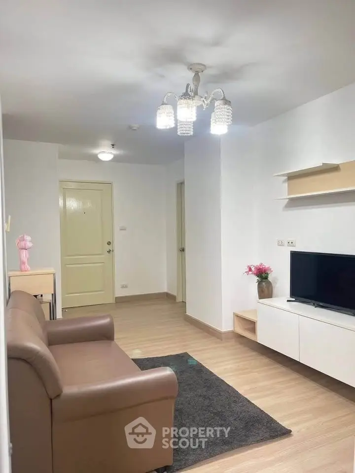 Modern living room with cozy sofa, stylish chandelier, and mounted TV in a bright apartment.