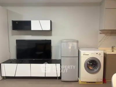 Modern living room with sleek furniture, TV, fridge, and washing machine for convenient urban living.