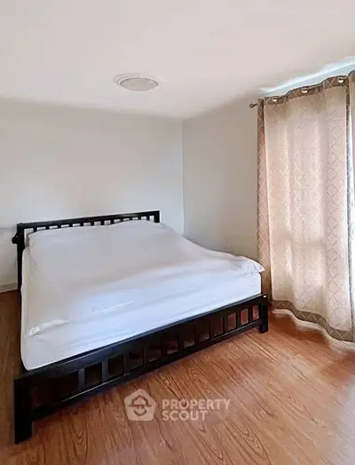 Spacious bedroom with wooden flooring and natural light through elegant curtains.