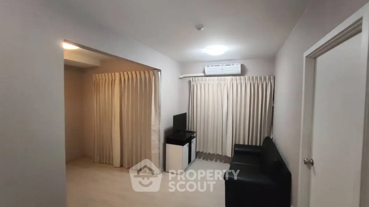 Modern living room with sleek black sofa and wall-mounted TV, featuring elegant curtains and air conditioning.