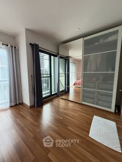 Spacious bedroom with wooden flooring and large mirrored wardrobe, featuring natural light from balcony access.
