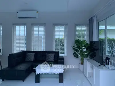Modern living room with sleek black sofa, large windows, and stylish decor.