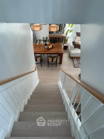 Modern staircase leading to a stylish dining and living area with wooden furniture and natural light.