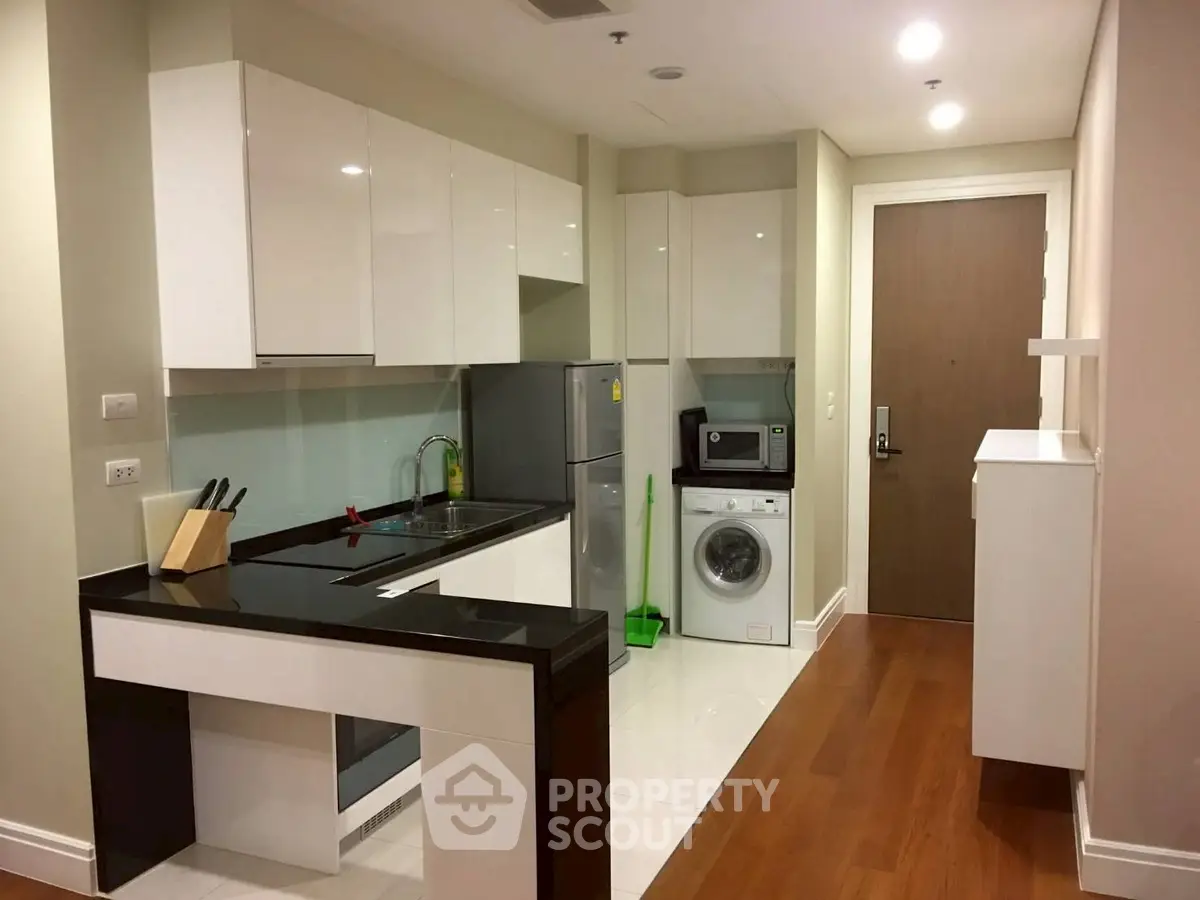 Modern kitchen with sleek cabinets, washing machine, and wooden flooring in a cozy apartment.