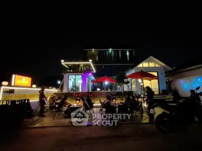 Charming nighttime view of a modern restaurant with outdoor seating and vibrant lighting.