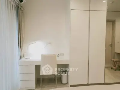 Modern bedroom with sleek white furniture and study area, featuring a minimalist design and ample natural light.