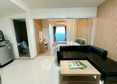 Modern studio apartment with ocean view, featuring sleek black sofa and compact kitchen area.