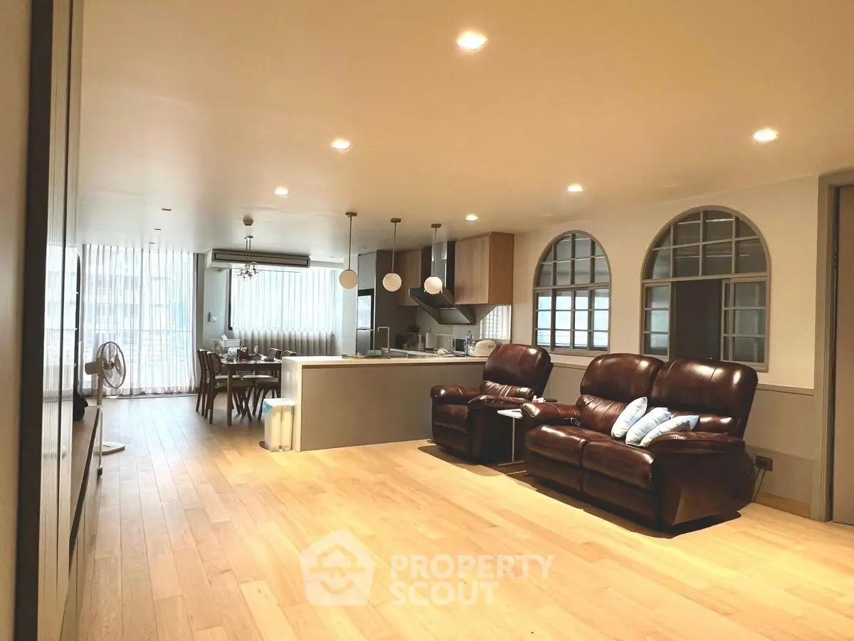 Spacious open-plan living room with modern kitchen and elegant dining area, featuring stylish lighting and wooden flooring.