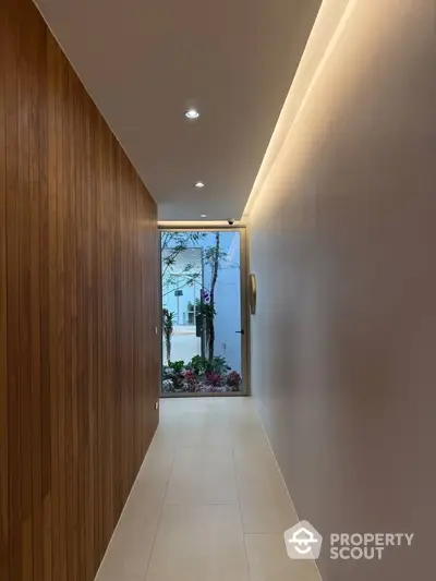 Elegant hallway with wooden paneling and modern lighting leading to a garden view.