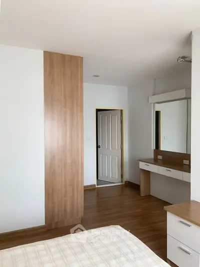 Modern bedroom with wooden flooring and built-in wardrobe, featuring a sleek dressing table and neutral decor.