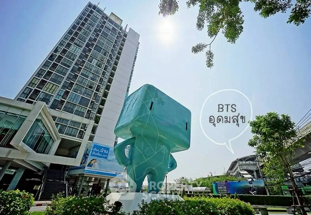 Modern high-rise building near BTS station with unique sculpture in vibrant urban setting.
