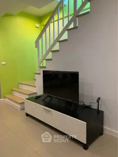 Modern living room with sleek TV stand and staircase, vibrant green accent wall, and contemporary design.
