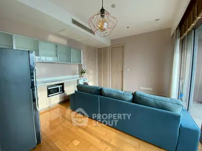 Modern living room with sleek kitchen and cozy blue sofa, featuring hardwood floors and stylish lighting.