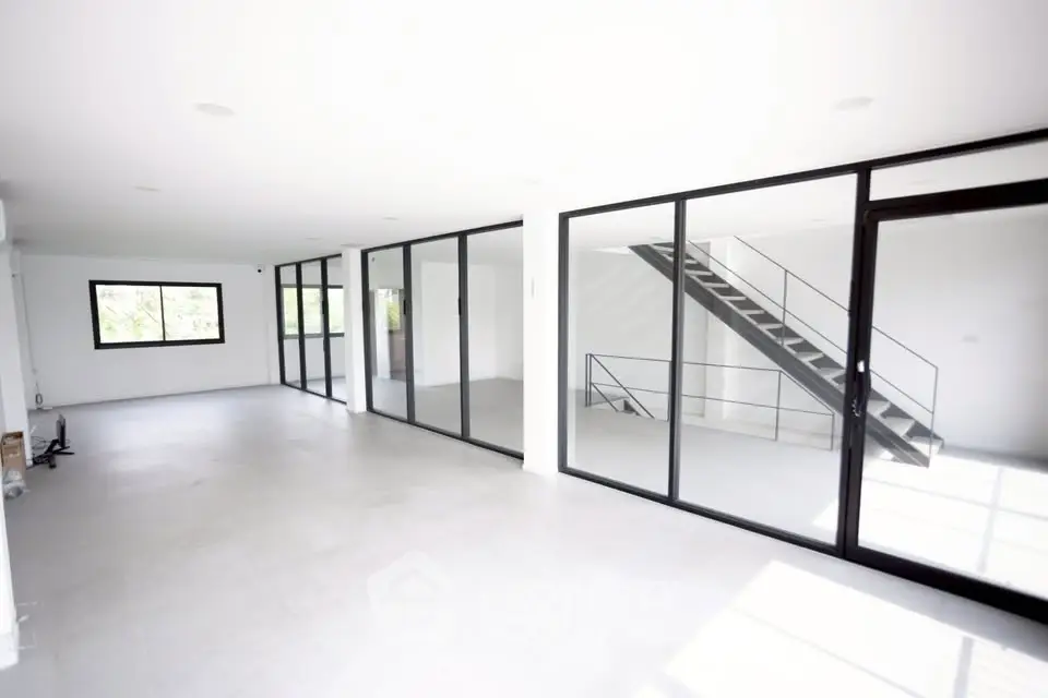 Spacious modern interior with large windows and sleek staircase, ideal for open-concept living.