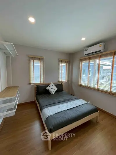 Modern bedroom with wooden flooring, large windows, and air conditioning unit.