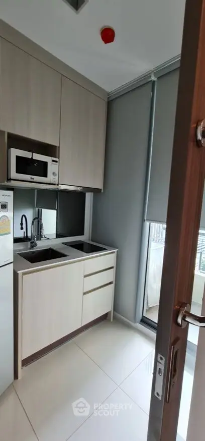 Modern compact kitchen with sleek cabinetry and built-in microwave, featuring a large window for natural light.