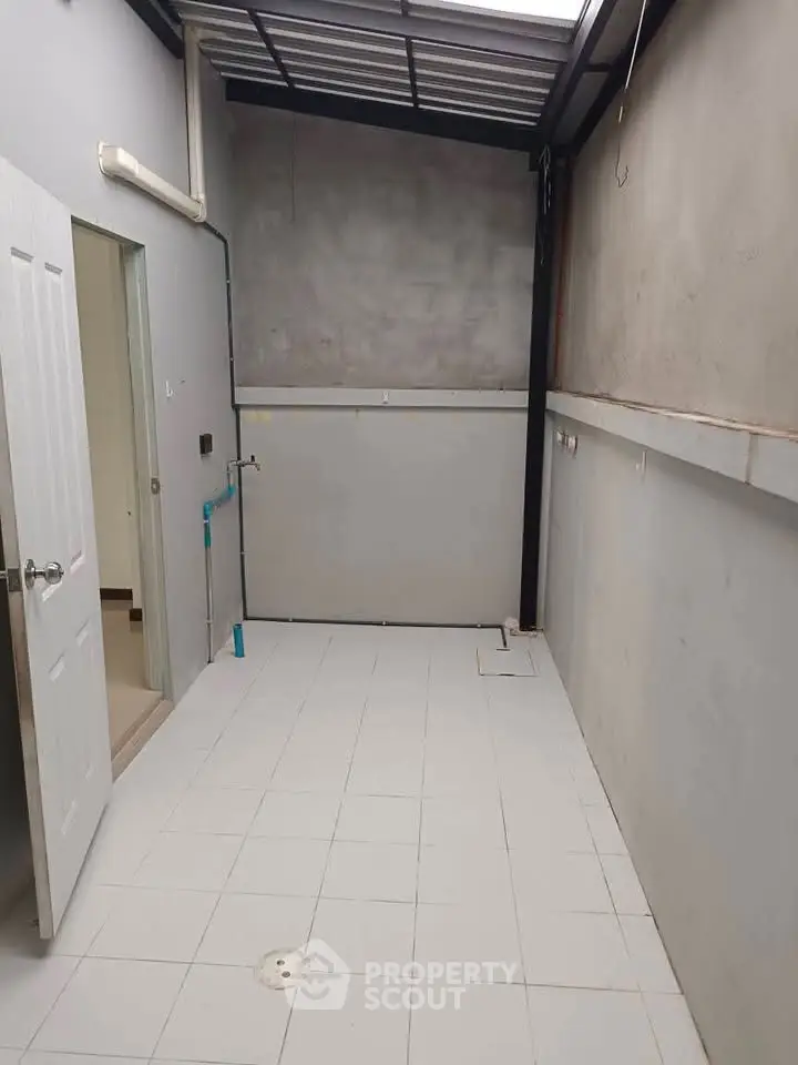 Spacious utility area with tiled flooring and open ceiling, ideal for laundry or storage.
